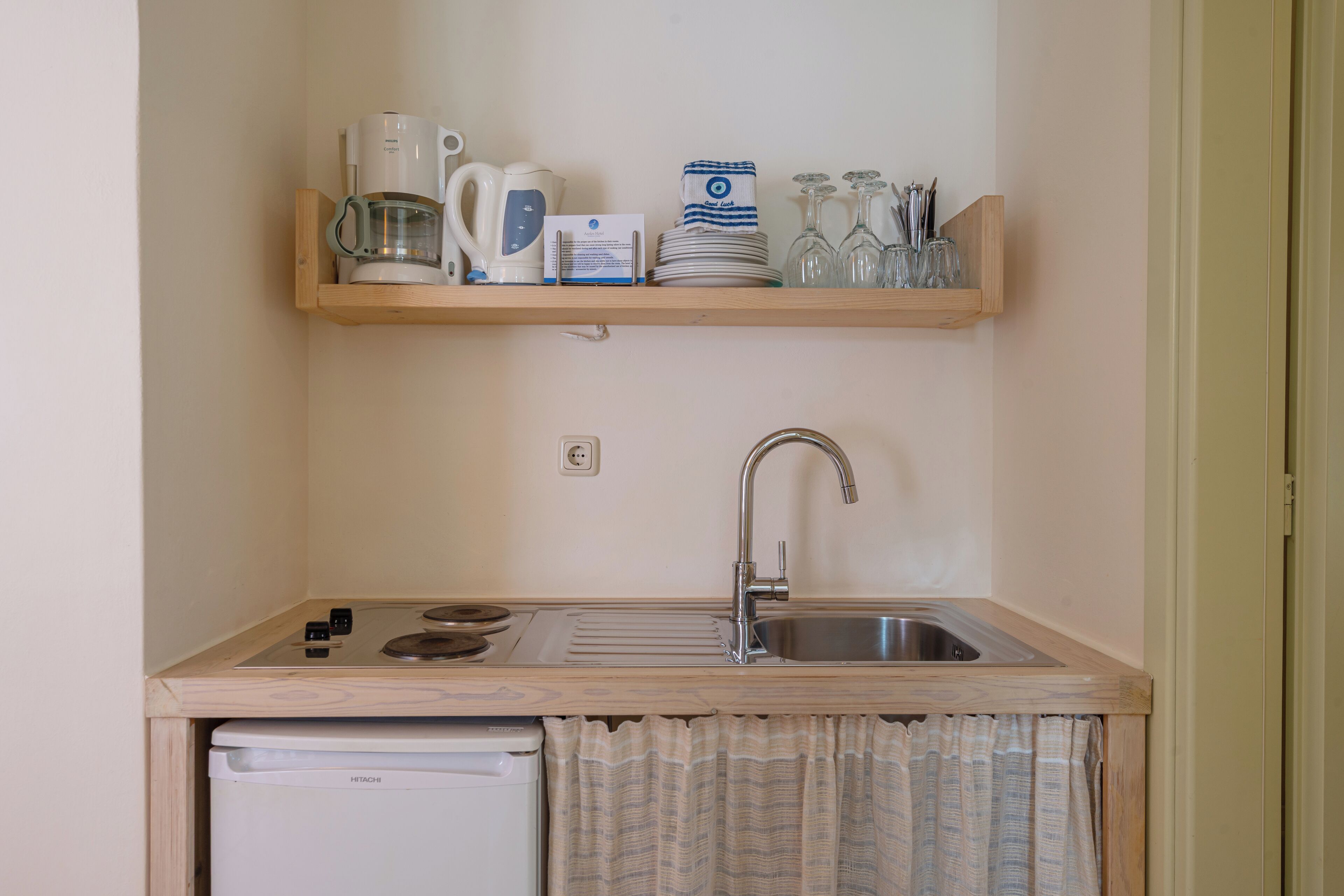 Una cocina compacta con un lavamanos, una cafetera, un hervidor y un refrigerador pequeño.