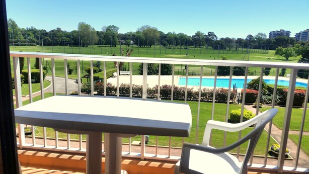 Un balcon avec une table et des chaises donnant sur une piscine et un espace vert aménagé en parc.
