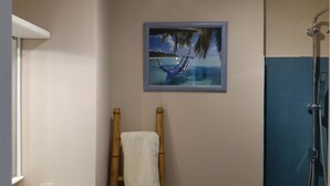 Une salle de bain avec un tableau encadré représentant un hamac sur une plage, une échelle en bois et une douche.