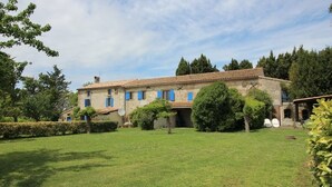 A stone building with a tiled roof, surrounded by a well-maintained lawn and trees.