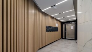 A modern hallway with a wooden panel wall, a black directory board, and a tiled floor. - Stylish Studio | Terrace, Air Conditioning, Center (Kraków)