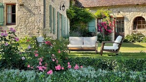 A stone building with a garden, a wooden bench, and a white sofa.