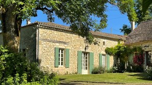 A stone building with green shutters, a grassy yard, and a tree.