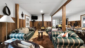 A cozy living room with plaid sofas, a fireplace, wooden walls, and a dining area. - Fentons Run, High Range, Southern Highlands (High Range)