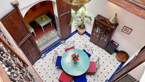 An indoor courtyard with a round table, chairs, a potted plant, and a decorative lamp. - Dar Malika · Traditional Fez house with spectacular view (Fes)