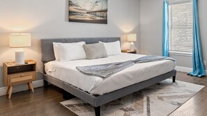 A bedroom with a bed, nightstands, a lamp, a painting, and a window with curtains.