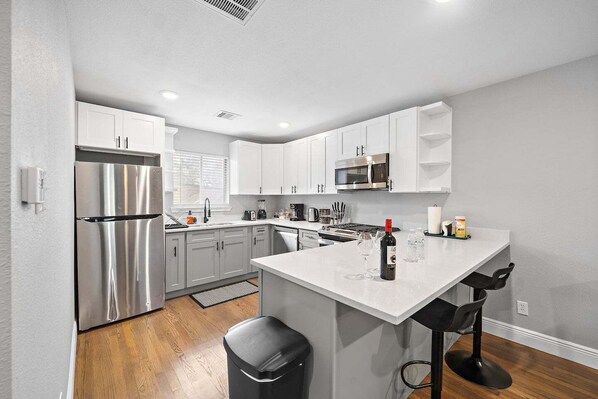 Una cocina moderna con armarios blancos, electrodomésticos de acero inoxidable y una isla central con taburetes de bar.