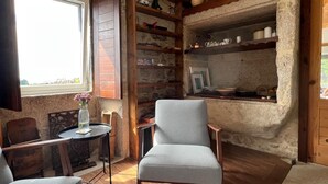 Ein gemütliches Zimmer mit Kamin aus Stein, Holzregalen, einem Esstisch und einem bequemen Sessel.