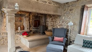Ein Zimmer mit Steinwänden, einem Kamin, einem grauen Sessel, einem weißen Sofa und einem kleinen Tisch mit einer Vase.