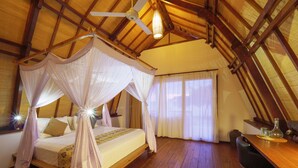 Un dormitorio con cama con dosel, suelo de madera, ventilador de techo y zona de comedor con mesa y sillas.