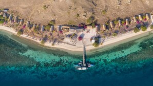 Vista aérea de un complejo turístico costero con playa, aguas cristalinas y un muelle con barcos.
