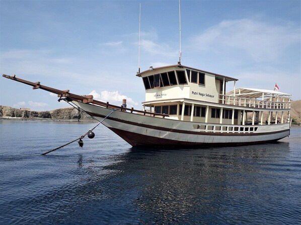 A traditional boat with a cabin and a covered upper deck, floating on calm water. - Komodo Resort (Komodo)