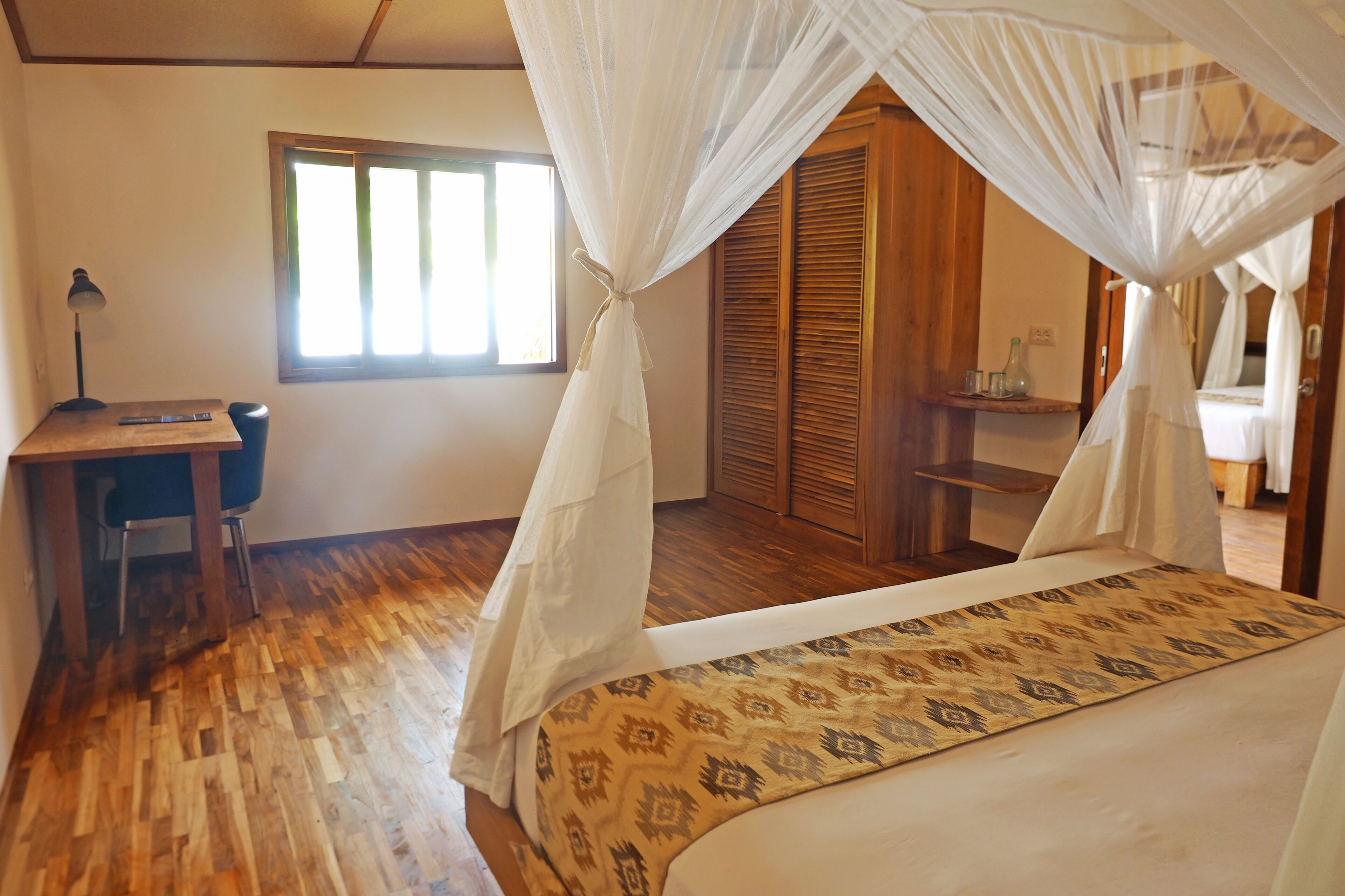 Un dormitorio con una cama, un escritorio y una silla. Hay una ventana y una puerta de madera.