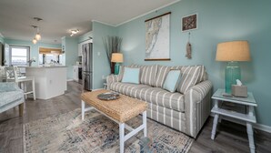 A modern living room with a striped sofa, a woven coffee table, and a small side table with a lamp.