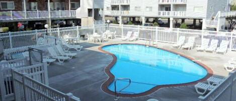 A pool area with lounge chairs and a fenced deck, surrounded by multi-story buildings.