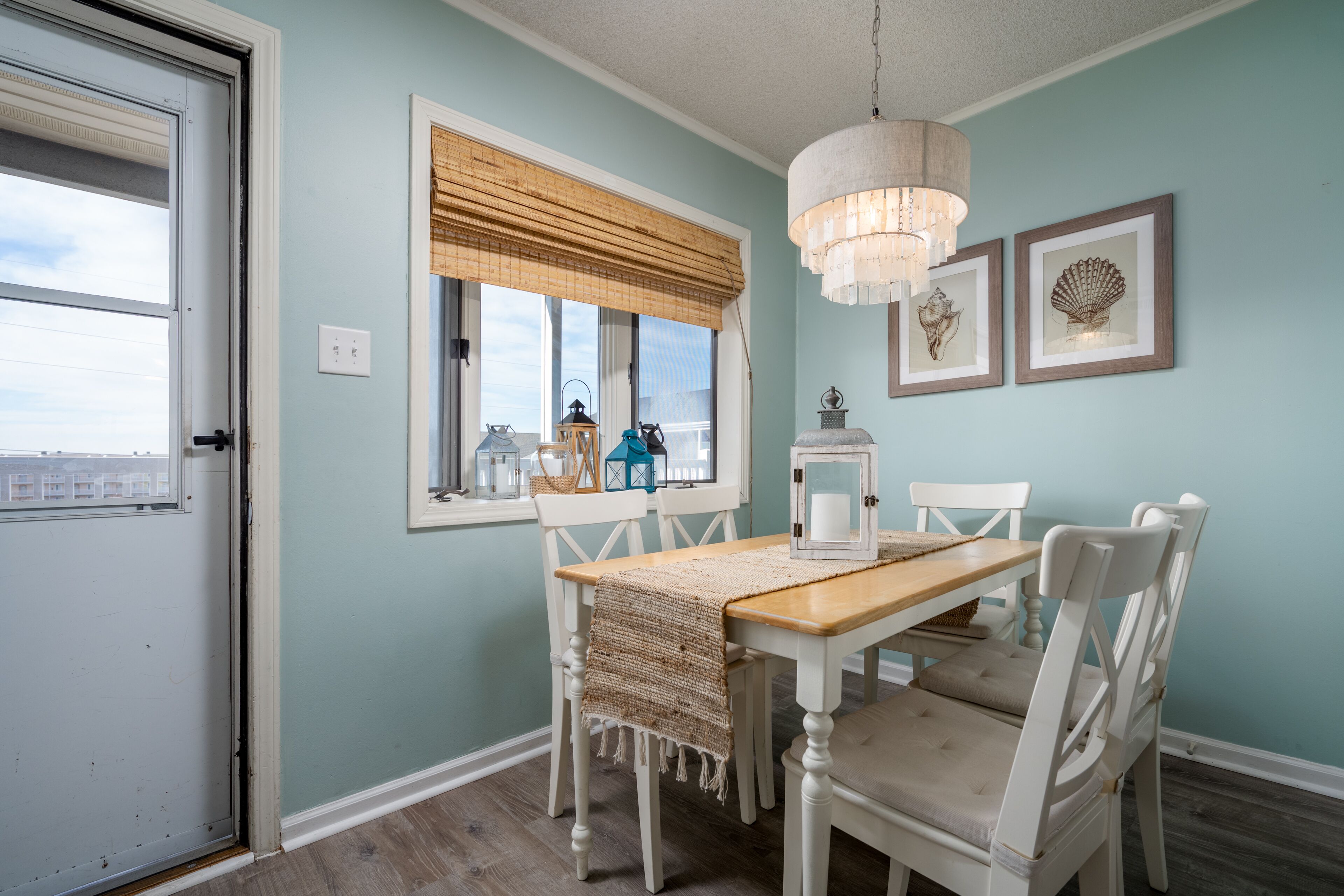 Een eetruimte met een houten tafel en witte stoelen, een kroonluchter en lijstwerken aan de muur.