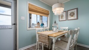A dining area with a wooden table and white chairs, a chandelier, and framed artwork on the wall.
