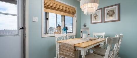Een eetruimte met een houten tafel en witte stoelen, een kroonluchter en lijstwerken aan de muur.