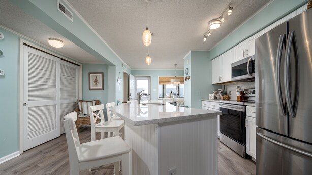 A modern kitchen with white cabinetry, a stainless steel refrigerator, and a central island with bar stools.