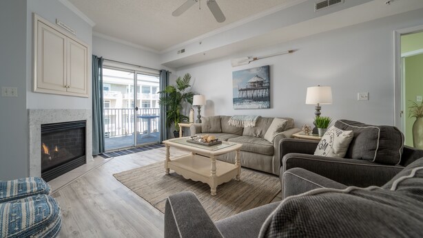 A living room with a fireplace, a ceiling fan, a sofa, a coffee table, and a large window with a view of a building.