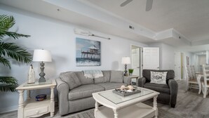 A living room with a grey sofa, a coffee table, and a painting of a pier.