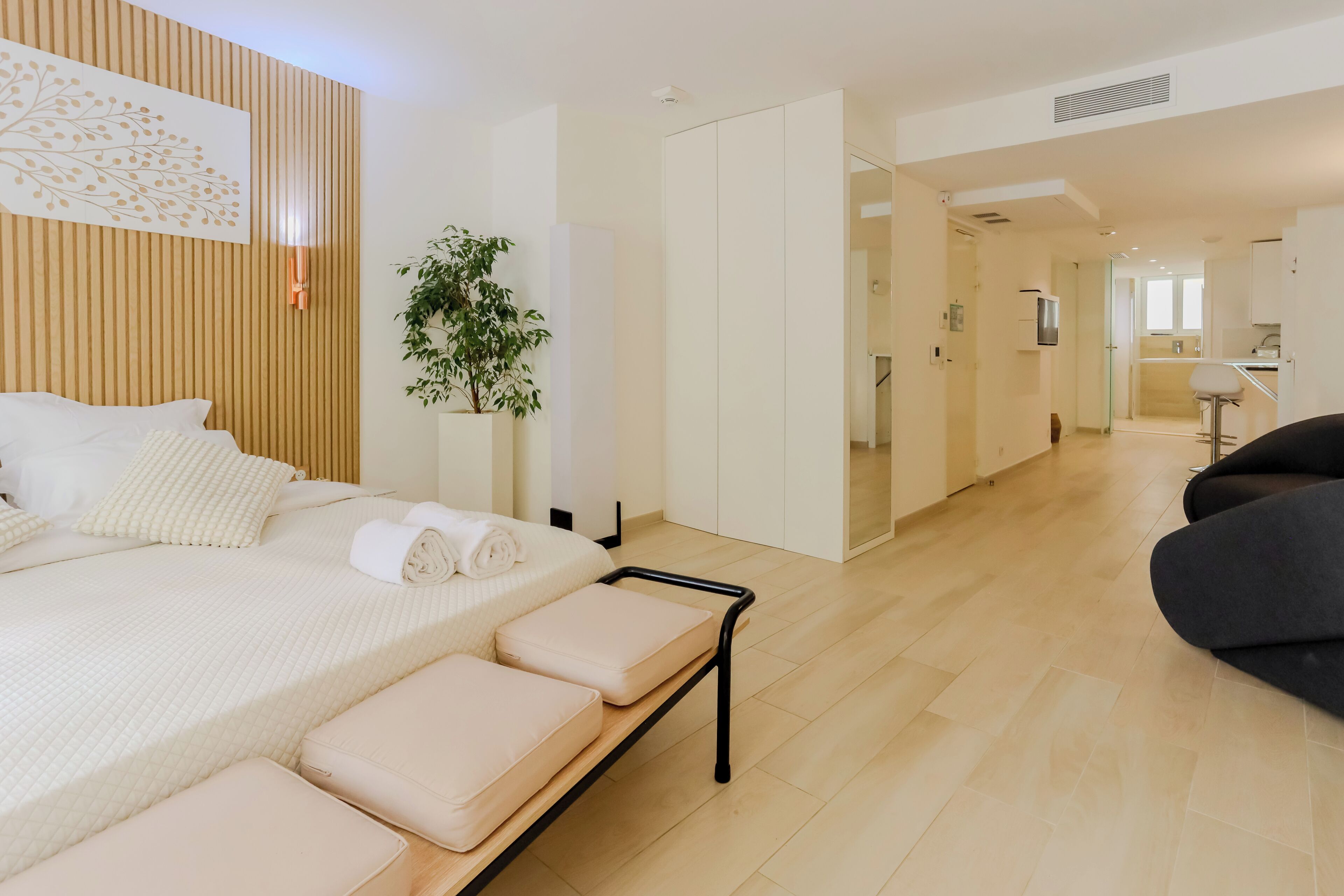 Un dormitorio moderno con una cama, mesitas de noche, una planta y vistas a la cocina.