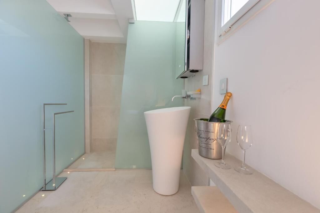 A modern bathroom with a glass shower enclosure, a white pedestal sink, and a champagne bottle in a silver bucket on the countertop.