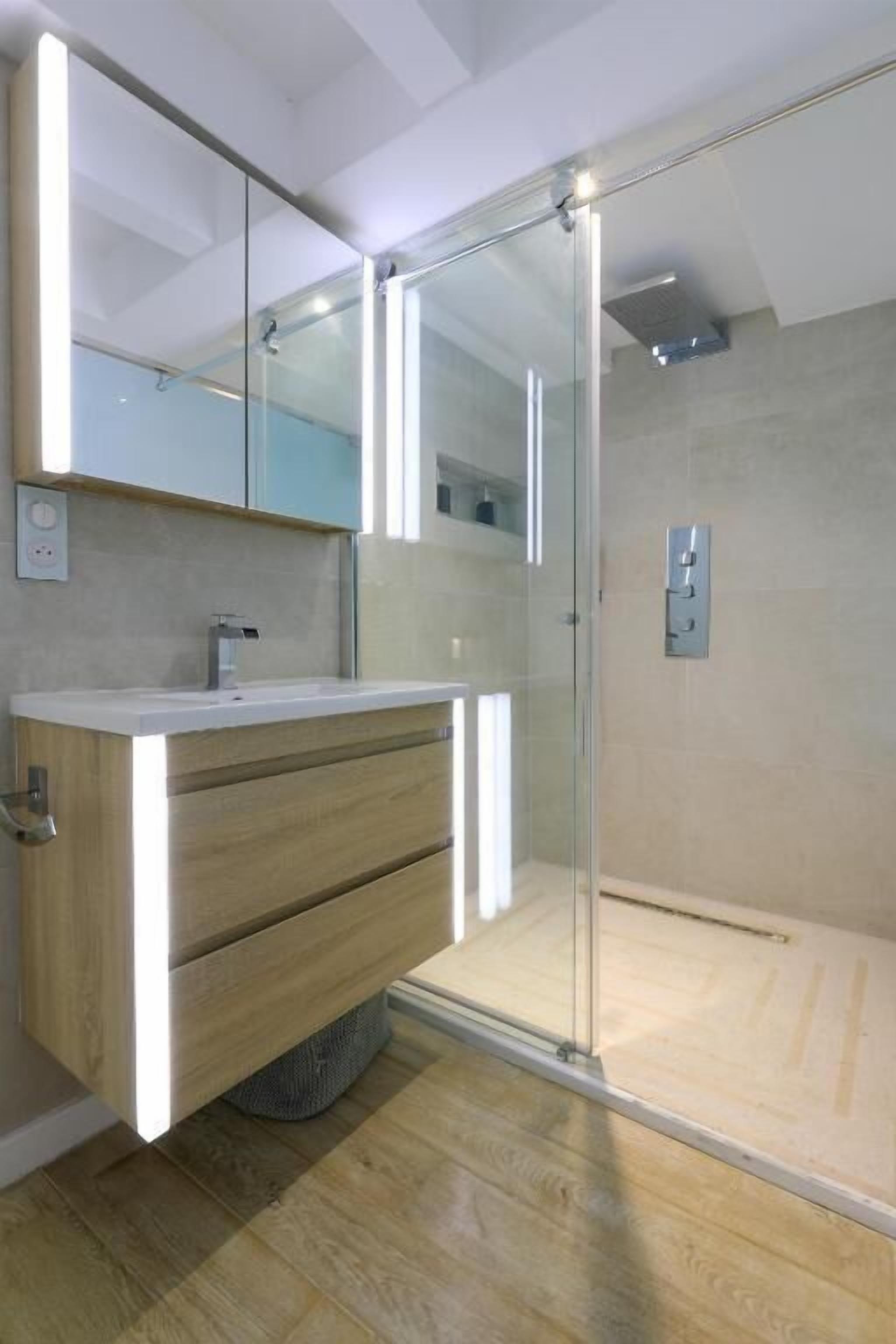 A modern bathroom with a glass shower enclosure, a wooden vanity, and a large mirror.