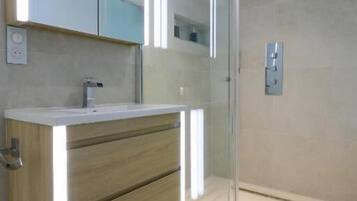 A modern bathroom with a glass shower enclosure, a wooden vanity, and a large mirror.