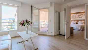 Una habitación de hotel moderna con balcón, un sofá blanco, una mesa de comedor y una cama con cabecera de madera.