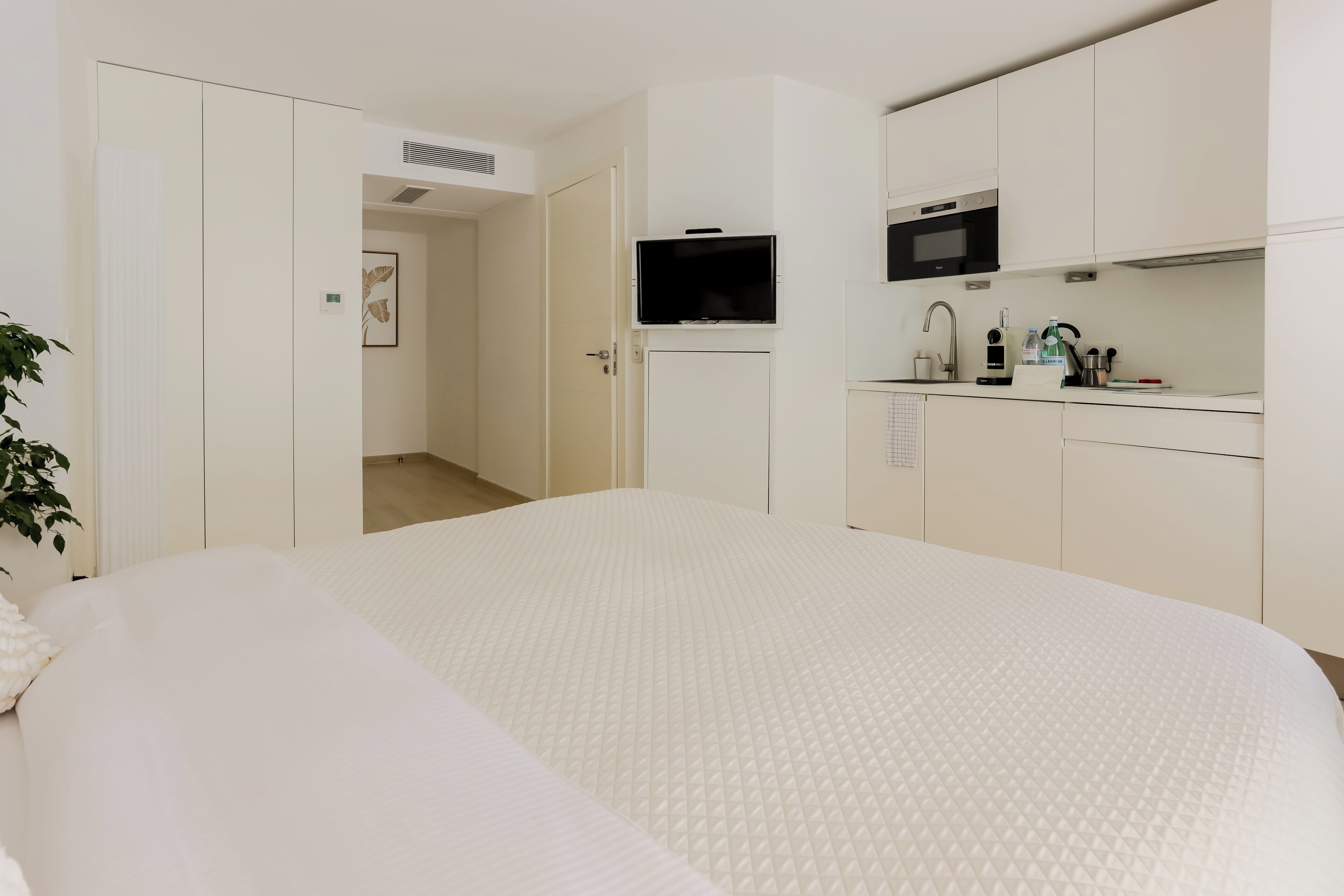 A hotel room with a large bed, a kitchenette with a microwave, and a door leading to a bathroom.