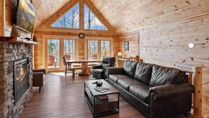 Ein Blockhaus-Interieur mit Kamin, Ledersofa, Holztisch und großen Fenstern.