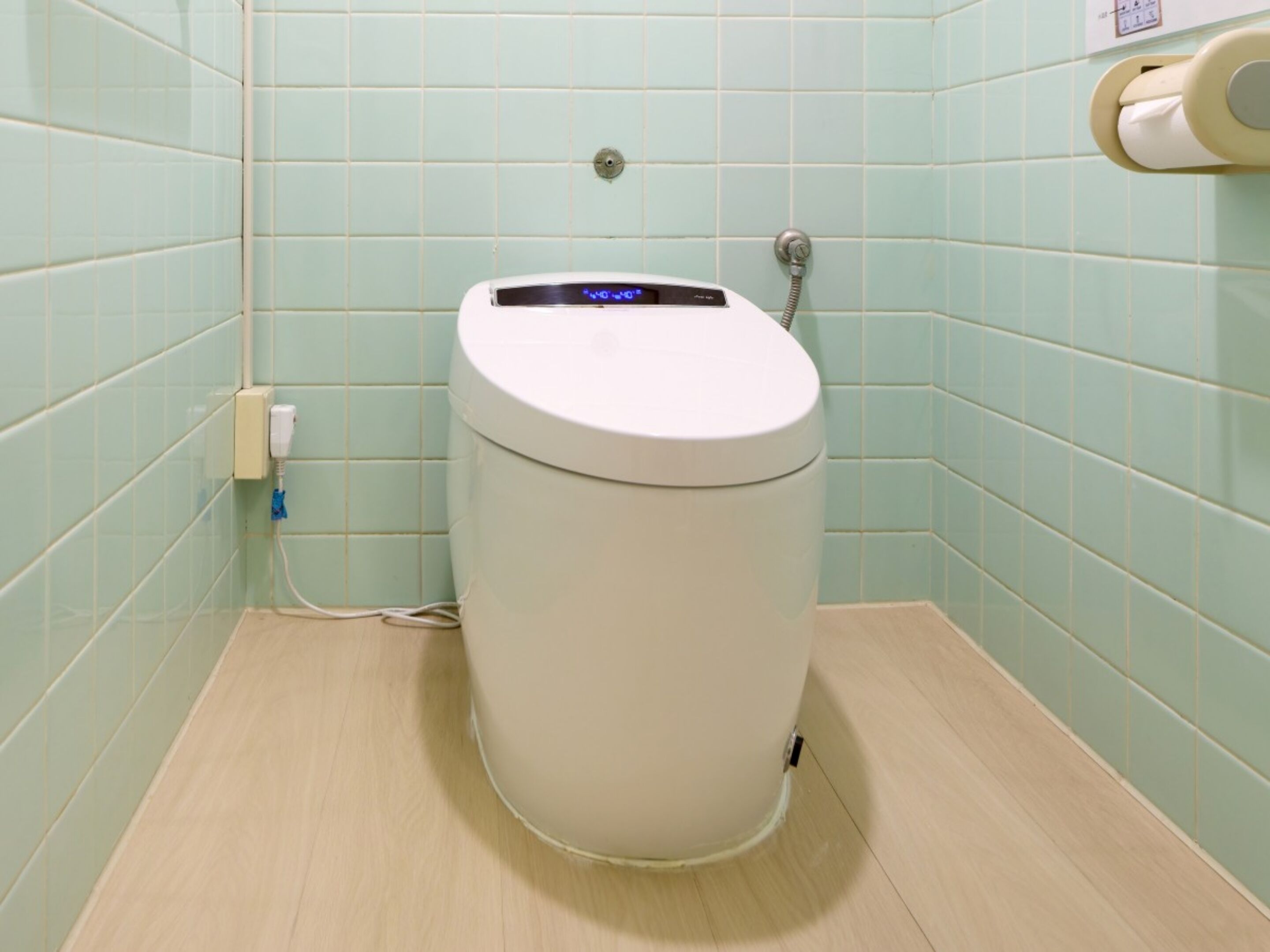 Eine Toilette mit digitaler Anzeige, einem Papierhandtuchspender und einem an der Wand befestigten Spülhebel.