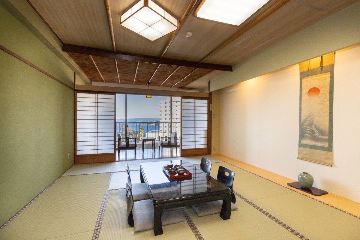 A traditional Japanese room with tatami flooring, a low table, and sliding doors leading to a balcony with a view.