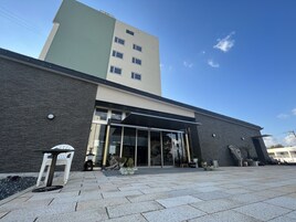 Un edificio moderno con entrada de vidrio, fachada de piedra y una estructura alta contigua.