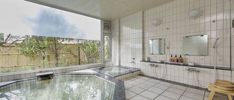 A modern bathroom with a large glass-enclosed hot tub, a shower area, and a vanity with a mirror and toiletries.