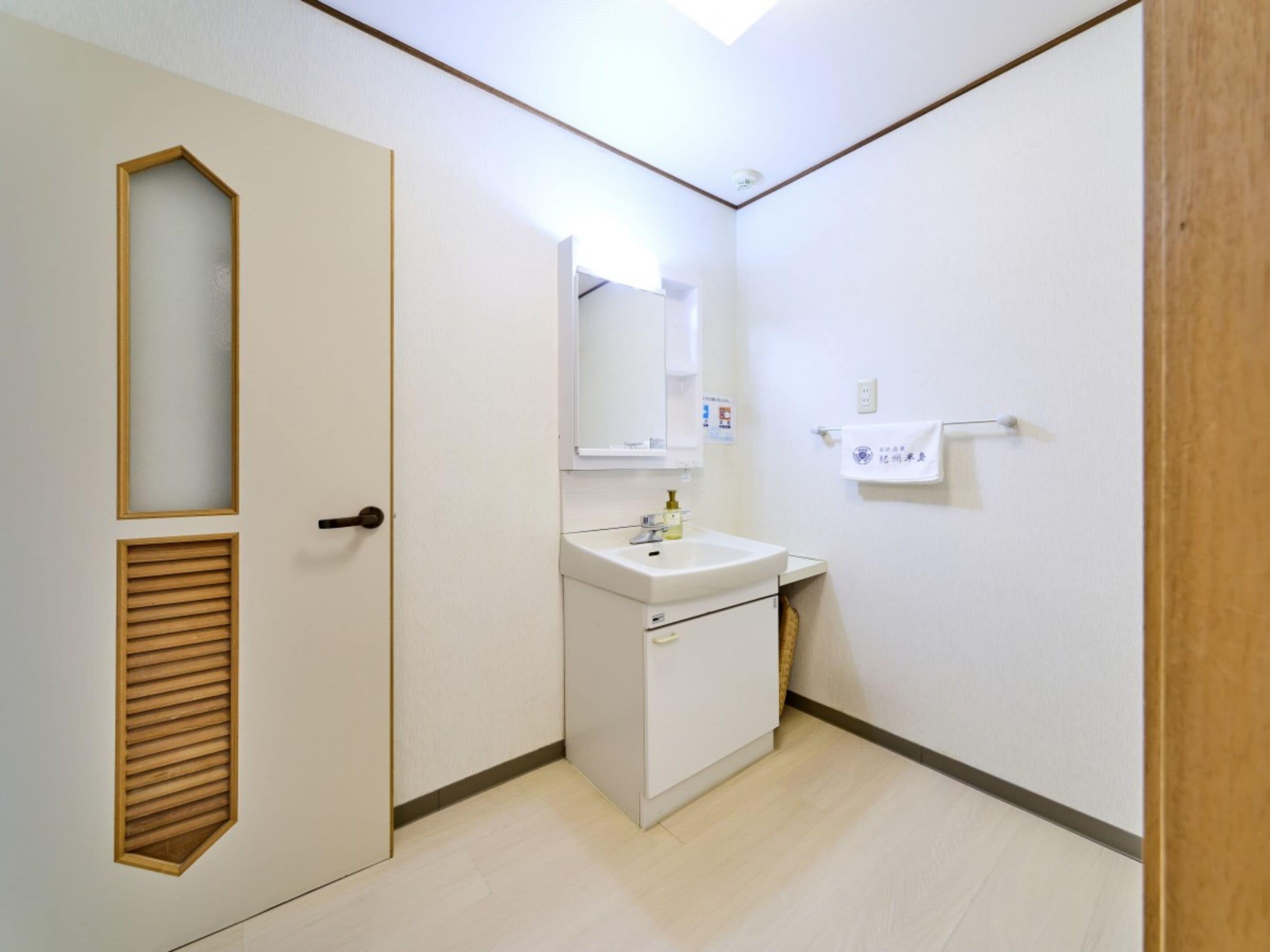 Une petite salle de bain propre, équipée d’un lavabo, d’un miroir et d’un porte-serviettes.