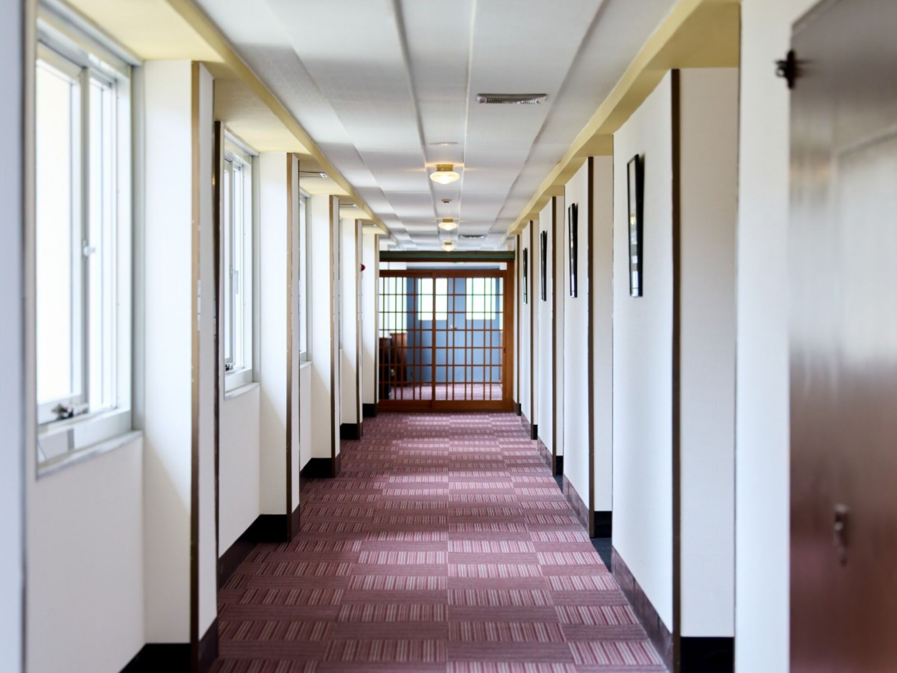 A long, narrow hallway with patterned carpet, white walls, and large windows on one side.