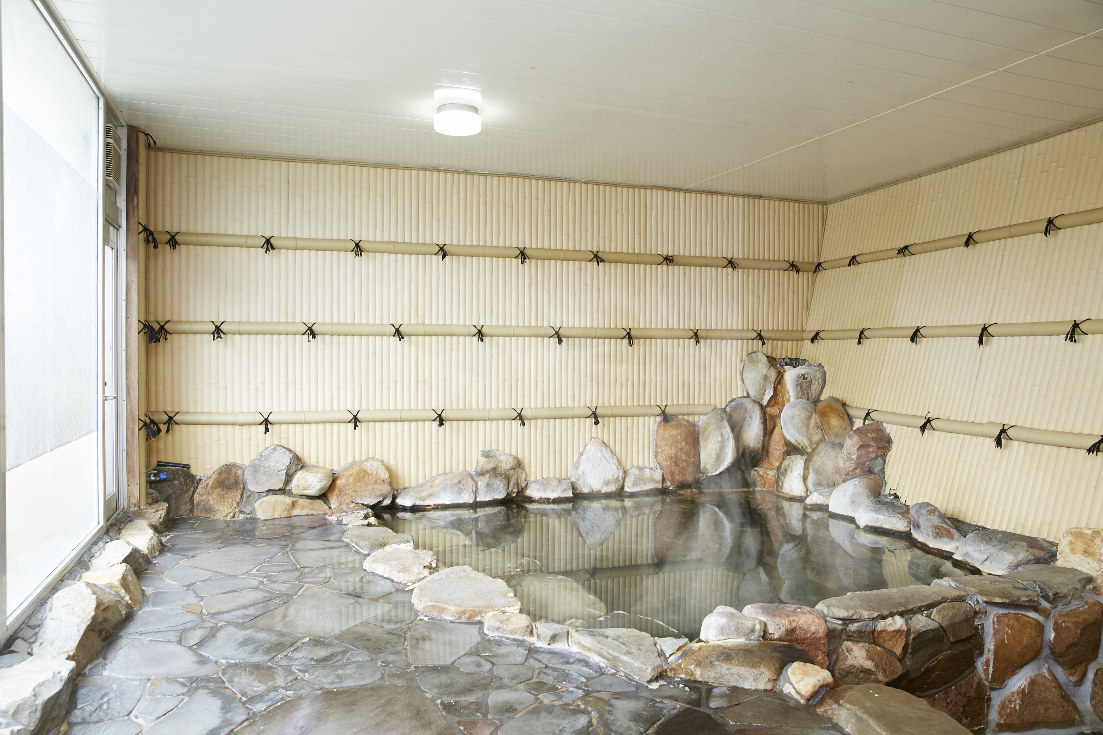 A traditional Japanese onsen with stone flooring and a rock-lined pool.