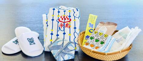 A table with a pair of white slippers, a patterned cloth, and a basket containing baby diapers and a card.