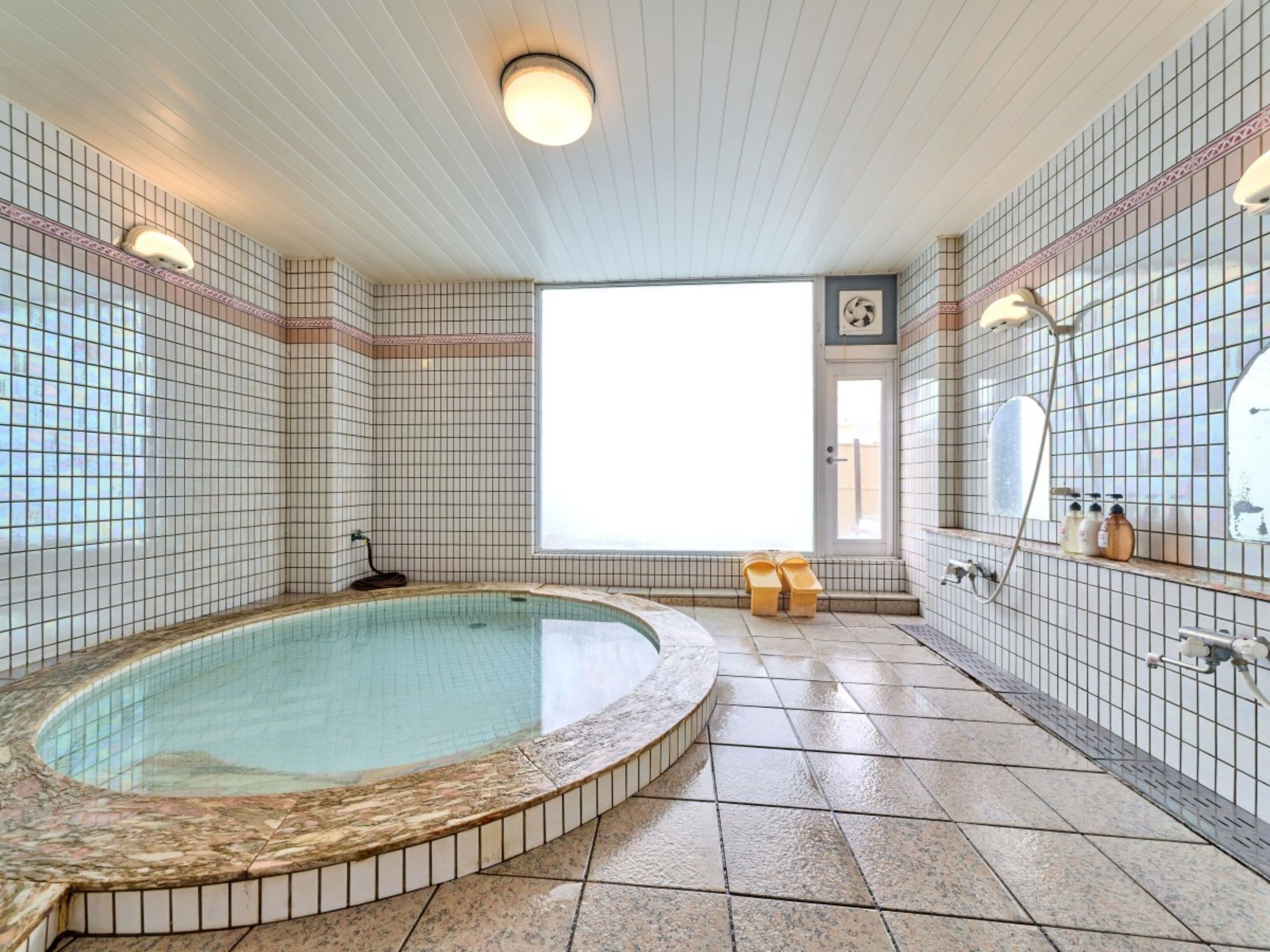A spa room with a hot tub, tiled walls, a window, and a shower area.