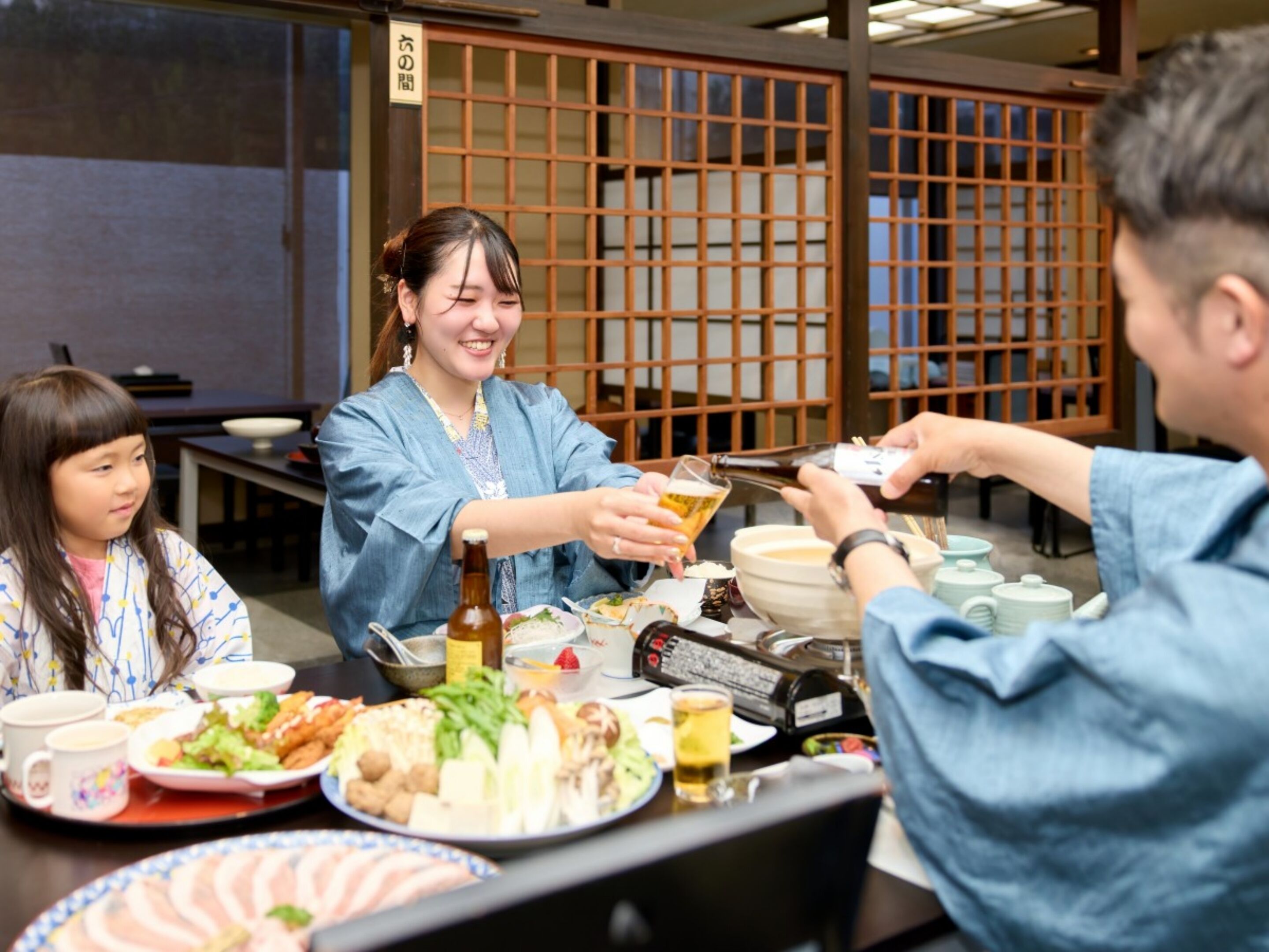 A group of people dining at a table with various dishes, a bottle, and a teapot.