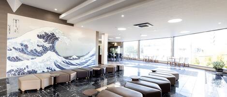 A modern hotel lobby with a large wave painting, plush seating, and a view through large windows.