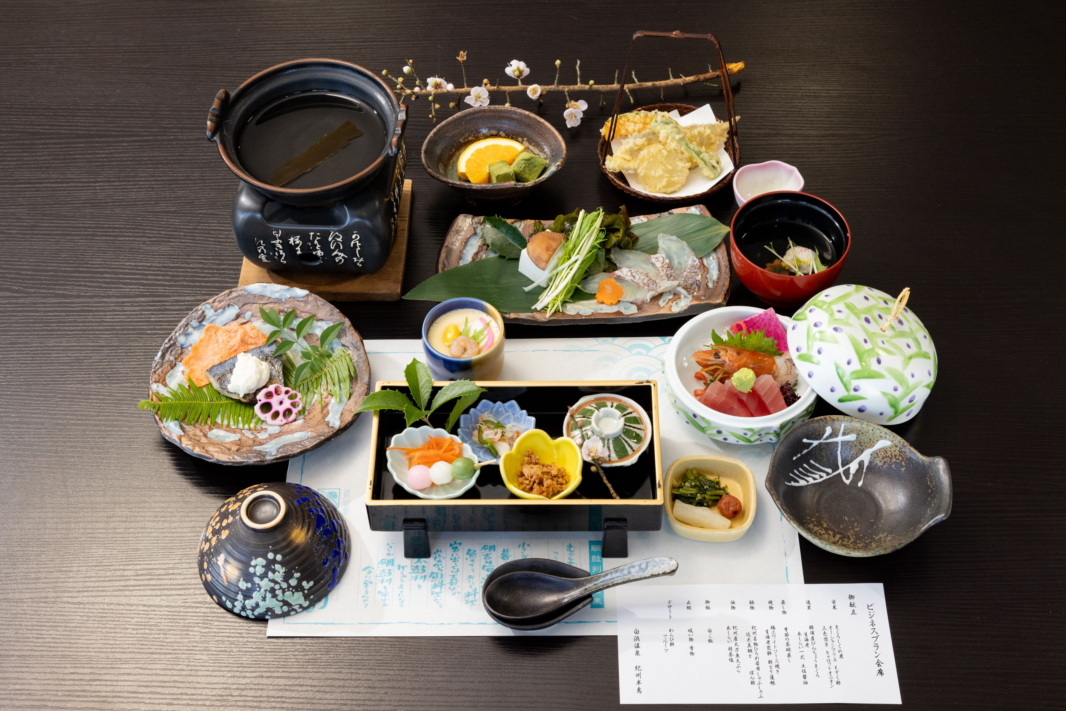 En traditionell japansk måltid serverad med olika rätter och serveringsredskap på ett träbord.