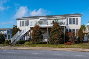 A two-story house with a front porch, a staircase, and a small garden with red flowering bushes. - Dog-Friendly house. Arctic Ave House: Sunny and bright beautiful 4 Bedroom 3 Full bathroom single home walking distance to the beach, Free WiFi, linens included. Remodel just in couple month. Great location, walk in to restaurants, coffee shop, Acme (Ocean City)