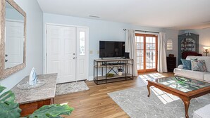 A living room with a television, a glass coffee table, a sofa, and a door leading to a balcony. - Dog-Friendly house. Arctic Ave House: Sunny and bright beautiful 4 Bedroom 3 Full bathroom single home walking distance to the beach, Free WiFi, linens included. Remodel just in couple month. Great location, walk in to restaurants, coffee shop, Acme (Ocean City)