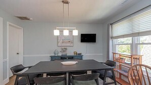 A dining area with a dark wooden table, six chairs, a chandelier, a flat-screen TV, and a bookshelf by the window. - Dog-Friendly house. Arctic Ave House: Sunny and bright beautiful 4 Bedroom 3 Full bathroom single home walking distance to the beach, Free WiFi, linens included. Remodel just in couple month. Great location, walk in to restaurants, coffee shop, Acme (Ocean City)