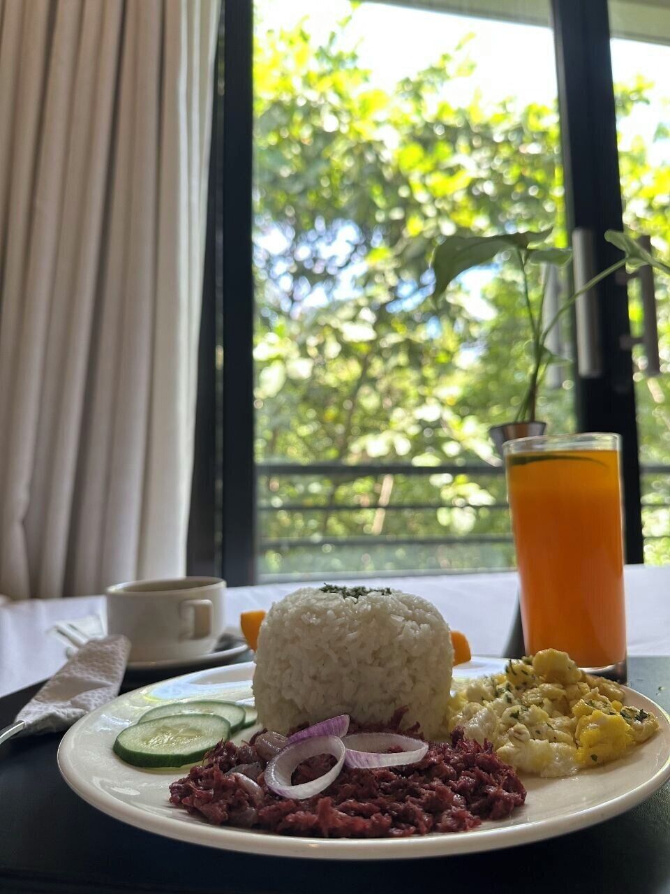 A plate with rice, a side dish, and a glass of orange juice on a table with a window view.