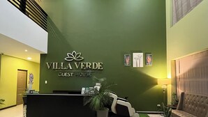 Zona de recepción de hotel con una pared verde, un mostrador, un sofá y una escalera.
