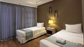 Habitación de hotel con dos camas, una mesita de noche, una lámpara y una ventana con cortinas.